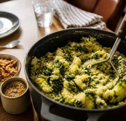 Pan huisgemaakte stamppot met stamper en smaakmakers op tafel