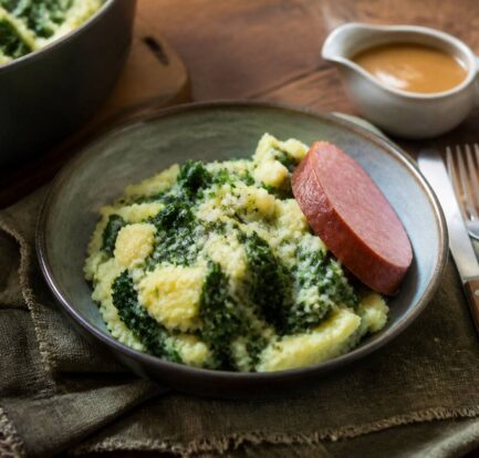 Kom stamppot met aardappelpuree, groente en rookworst op een houten tafel